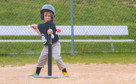 A young boy focuses on a baseball atop a tee during a baseball game.
