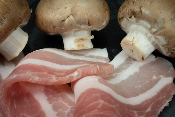 Raw dry-cured back bacon and mushrooms Close up raw dry-cured back bacon and mushrooms on a dark stone serving plate twisted bacon stock pictures, royalty-free photos & images