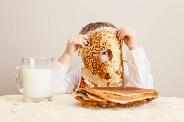 der urlaub von maslenitsa. das kind nahm einen pfannkuchen. das kind schaut durch das loch in den dreck. großer gebackener pfannkuchen - shrove tuesday stock-fotos und bilder