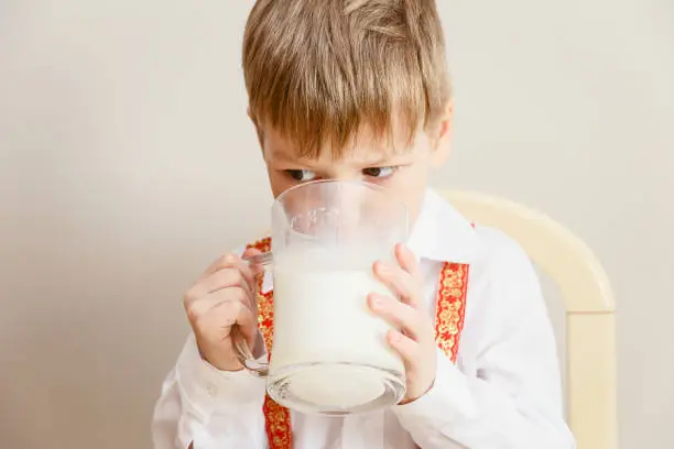 little boy in white shirt drinking milk from huge transparent glass mug on white background
