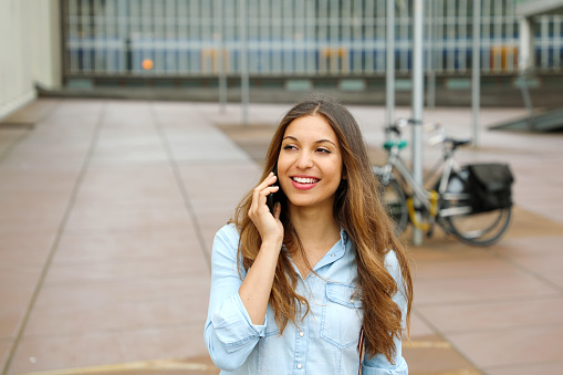 Thoughtful Young Woman Talking On Phone While Standing On Footpath In City