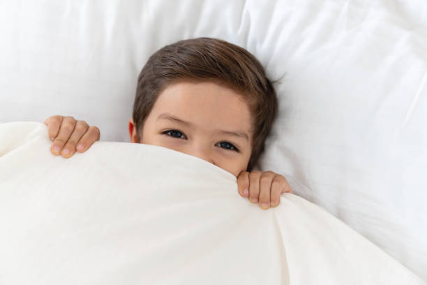 Happy boy at home lying in bed under the covers