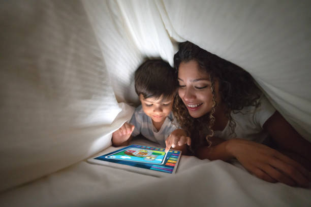 madre e hijo jugando en una tableta digital en la cama - online game fotografías e imágenes de stock