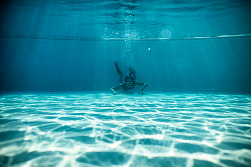 Teenage girl swimming underwater in pool near the bottom of the pool.
Nikon D850