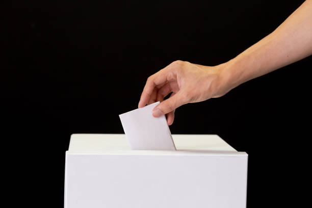 Close-up of human hand casting and inserting a vote and choosing and making a decision what he wants in polling box - politics and democracy concept stock photo