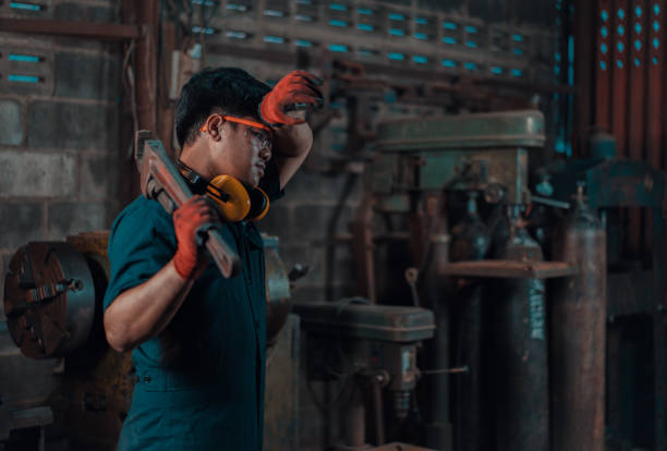 Mechanical engineer taking a break and wiping sweat off his forehead while resting a pipe wrench on his shoulder during his work shift stock photo