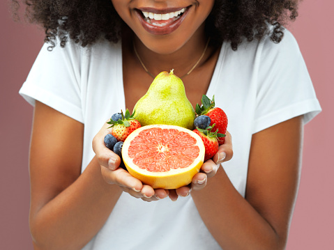 Cropped studio shot of an young woman holding fruit against a pink background