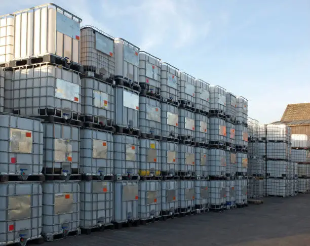 Photo of used metal framed intermediate bulk containers stacked on pallets waiting to be cleaned or recycled in an industrial yard