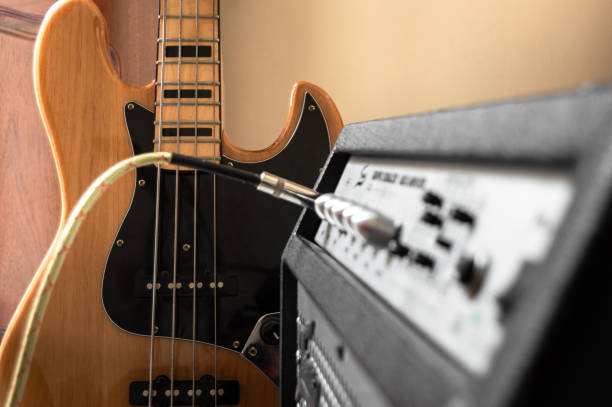 Vintage electric bass of four strings plugged into speaker in interior place. Amplifier with blur effect with bass in the background. Playing in home. Vintage electric bass of four strings plugged into speaker in interior place. Amplifier with blur effect with bass in the background. Playing in home. bass guitar stock pictures, royalty-free photos & images