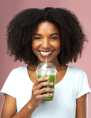Studio shot of an attractive young woman drinking green juice against a pink background