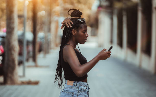 black girl using cellphone outdoors - braids african descent women pensive imagens e fotografias de stock