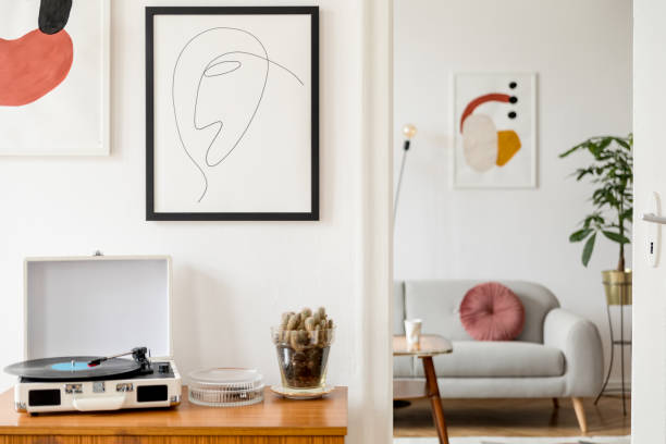 intérieur vintage et rétro de la salle de séjour avec commode design, enregistreur de vinyle, cactus et maquettes affiches cadres sur les murs blancs. chambre confortable avec parquet en bois brun et des plantes. - designer living room brown white photos et images de collection