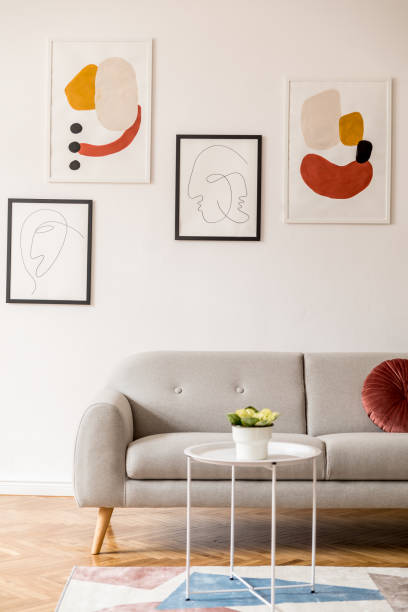 istock Stylish vintage decor in a spacious flat interior with design grey sofa, coffee table and posters on the wall. Brwon wooden parquet, stylish carpet and plants. Bright living room. 1132529263