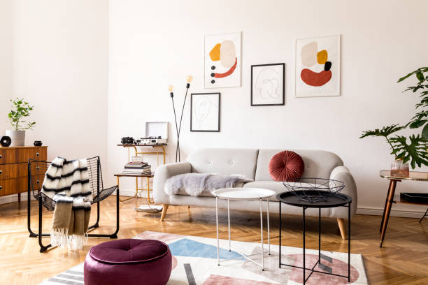 istock Elegant vintage decor in a spacious flat interior with design grey sofa, armchair, retro commode and posters on the wall. Brwon wooden parquet, stylish carpet and plants. Bright living room. 1132529427