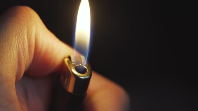 Close up shot of lighter on the man hand. Macro shot of Igniting lighter in the dark