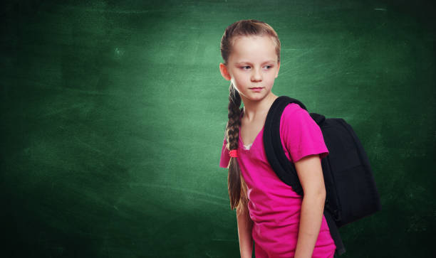 istock Cute Girl With Backpack Looking Away While Standing Against Blackboard 1132537502
