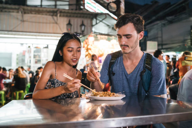 giovane coppia che cena insieme al mercato notturno - thailand thai culture thai cuisine pad thai foto e immagini stock