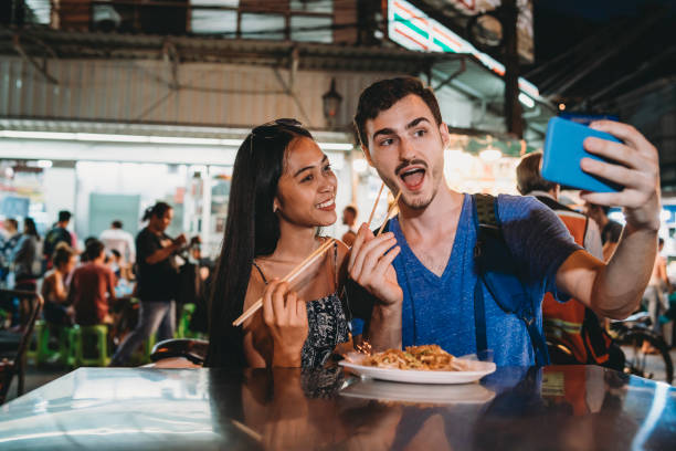 pareja joven cenando juntos en el mercado nocturno y tomar un selfie - khao san road fotografías e imágenes de stock