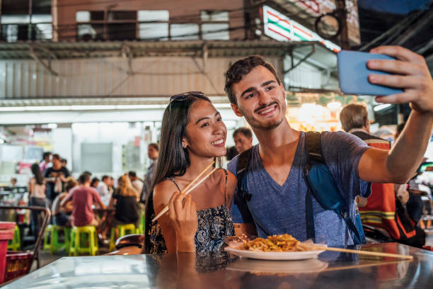 giovane coppia che cena insieme al mercato notturno e si fa un selfie - thailand thai culture thai cuisine pad thai foto e immagini stock