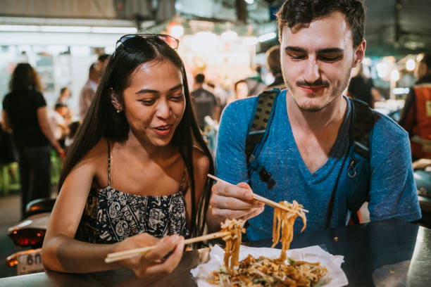 junges paar beim gemeinsamen abendessen auf dem nachtmarkt - eating men food chopsticks stock-fotos und bilder