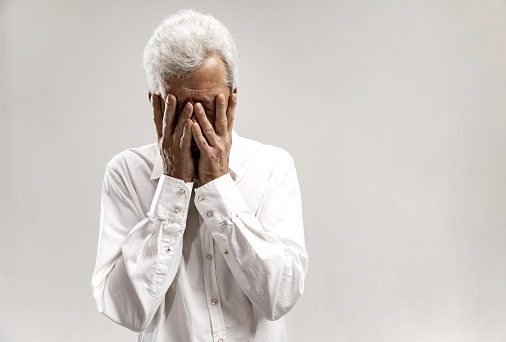 Portrait of upset old man rubbing his eye while crying. Isolated on grey background
