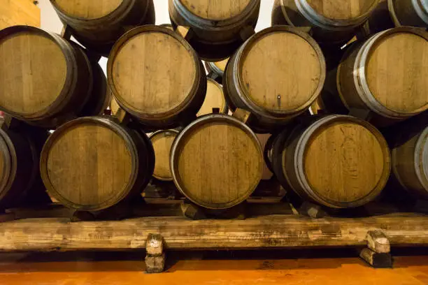 Wine barrels stacked in a cellar at winery. Wooden barrels of wine in vineyard. A lot of wine barrels stacked in a cellar.