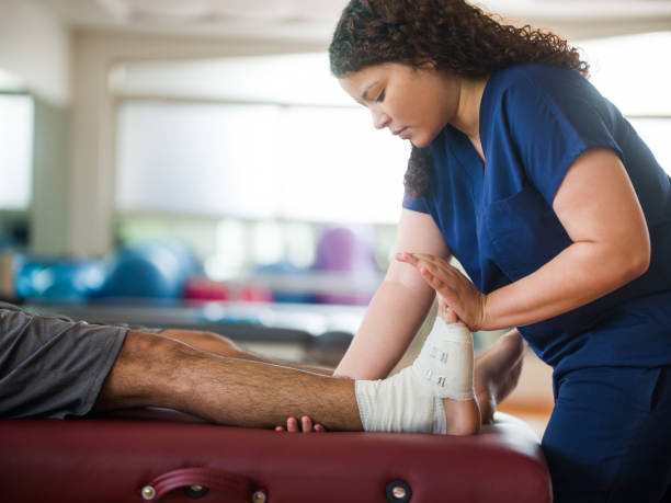 Occupational therapist holding leg and foot of patient A female occupational therapist holding leg and foot of a male patient with a bandage in his ankle. sports medicine photos stock pictures, royalty-free photos & images