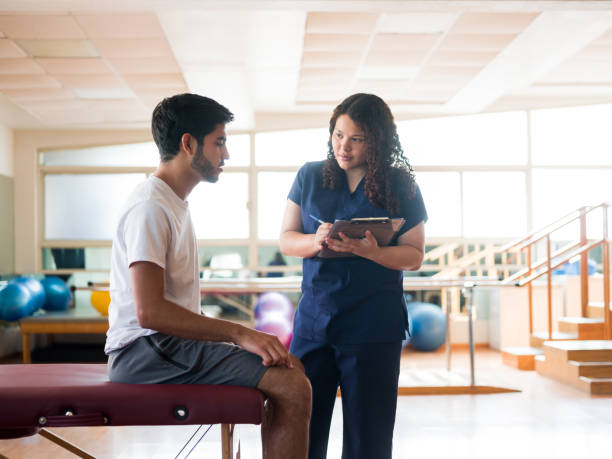 istock Physical therapist holding clipboard and standing next to patient 1132546195