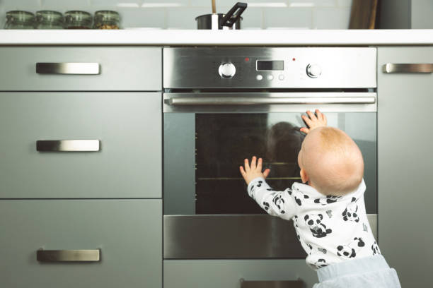 маленький ребенок, играющий с электрической плитой на кухне. безопасность ребенка на кухне - child proof стоковые фото и изображения