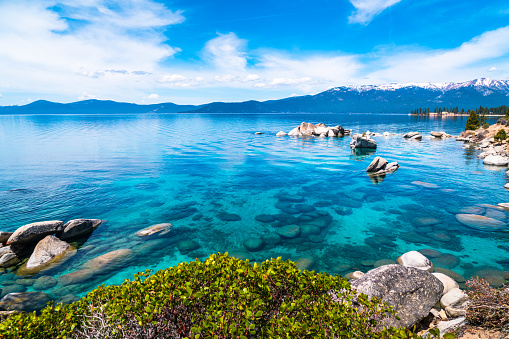 Sierra Nevada Mountains loom in the background and Huge boulders spotted along the turquoise Turquiose Dream Like Landscape shores of Lake Tahoe California