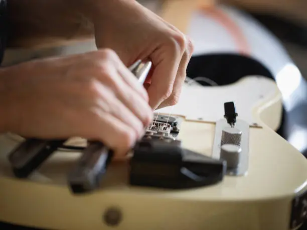 Guitar player doing telecaster type electric guitar maintenance, setting new strings