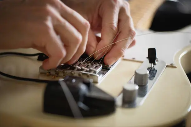 Guitar player doing telecaster type electric guitar maintenance, setting new strings