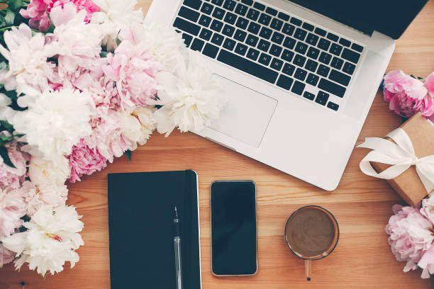 istock Stylish phone with empty screen, laptop, coffee cup, notebook,gift with pink and white peonies on table flat lay with space for text. Freelance concept. Stylish working place. 1132563502