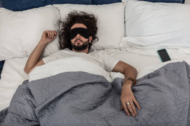 Nice sleepy tired man lying on the bed Perfect relaxation. Nice sleepy man lying on his bed while wearing a sleeping mask sleep eye mask stock pictures, royalty-free photos & images
