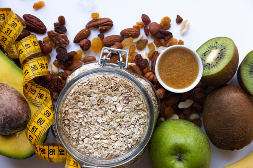 Healthy breakfast ingrediens. Homemade granola in open glass jar, honey, nuts, fruits, yellow tape-lane on white background