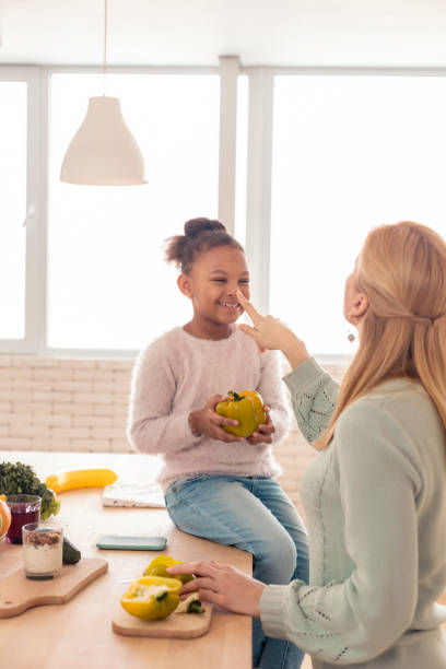 istock Cute cheerful girl holding pepper while helping mother cooking 1132579406