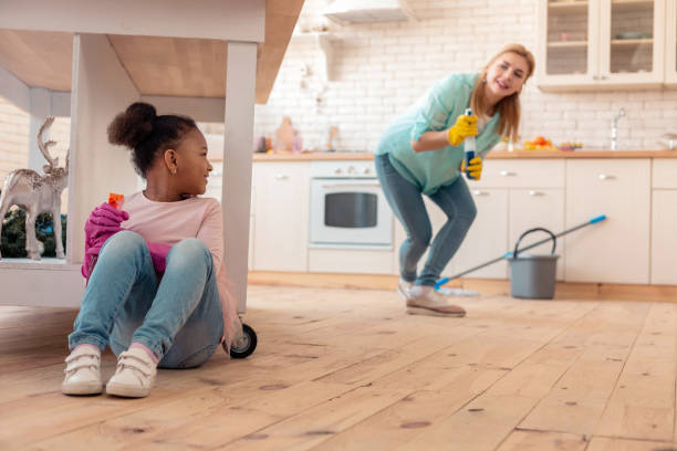 istock Cute curly daughter hiding under table while cleaning flat with mom 1132579537