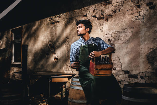 maître brasseur assis sur un tonneau en bois et tient un verre de bière artisanale, se détend après le travail. - after work beautiful people beer beer bottle photos et images de collection