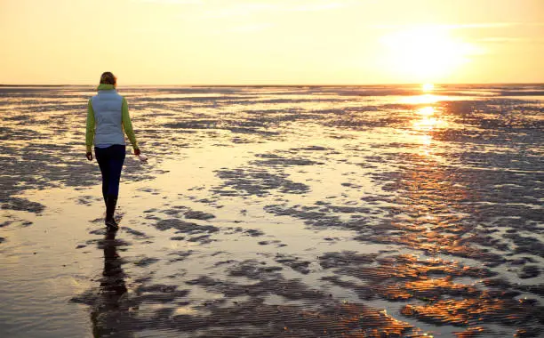 A young woman walks across the mudflats of the Waddensea at low tide, The Netherlands