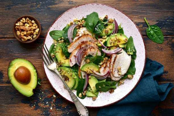 Spinach salad with grilled chicken fillet, avocado and walnuts Spinach salad with grilled chicken fillet, avocado and walnuts on a plate over dark wooden background.Top view with copy space. paleo diet photos stock pictures, royalty-free photos & images