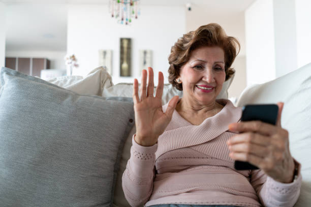 beautiful senior woman relaxing on couch on a video call greeting looking very happy - video call imagens e fotografias de stock