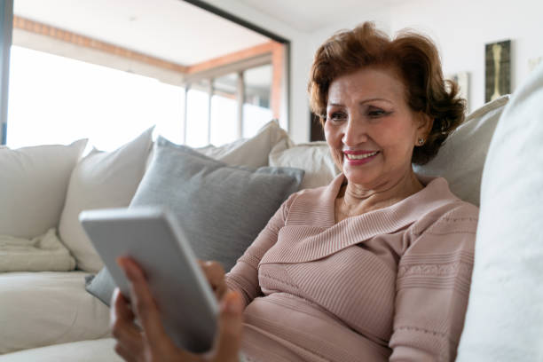 istock Happy senior woman looking at photos on digital tablet while relaxing on couch 1132625498