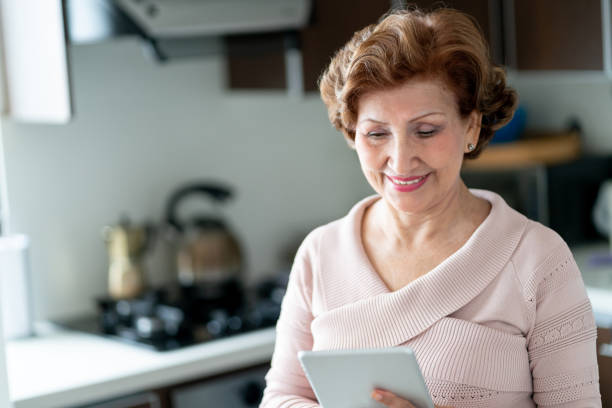 istock Latin american beautiful senior woman looking at tablet while standing at the kitchen 1132625509