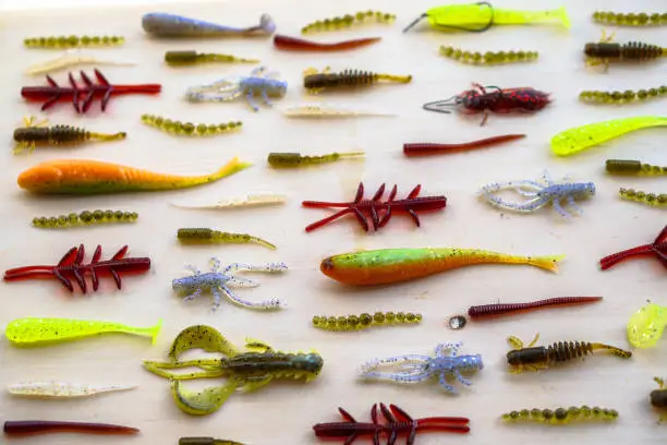 Photo of Colorful silicone fishing baits with plummets on wooden table. Various fish and worms and crayfish. Toned image and top view. Stock background, photo