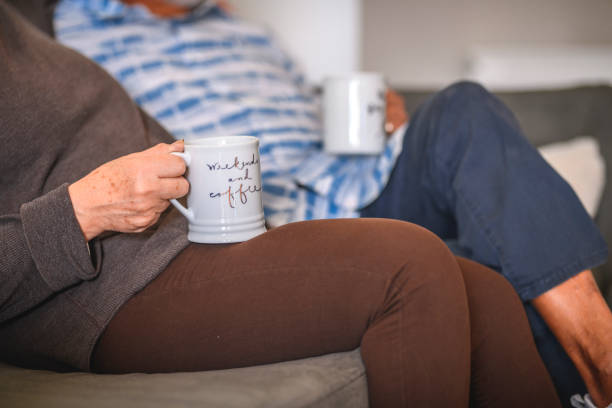 couples aînés de sourire retenant des tasses de café sur le sofa - senior adult comfortable relaxation latin american and hispanic ethnicity photos et images de collection