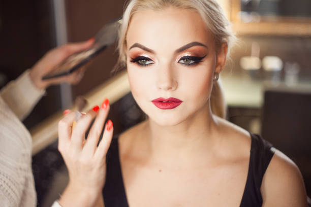 Beautiful young blonde. Makeup artist makes a stylish makeup. Close-up dark background