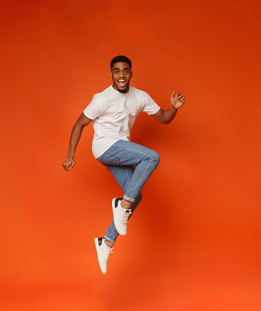 Funny portrait on young african-american man in humorous jump on orange background