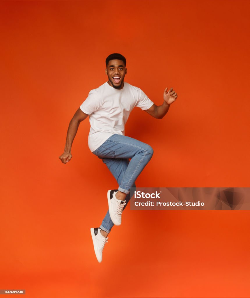 Excited african-american man jumping on orange background Funny portrait on young african-american man in humorous jump on orange background Jumping Stock Photo