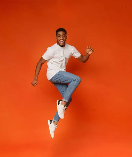Photo of Excited african-american man jumping on orange background