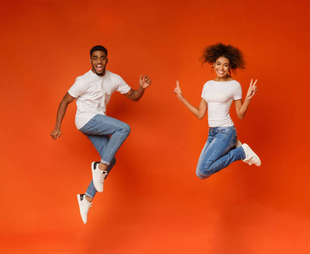 Excited black couple jumping on orange background Excited african-american couple jumping, having fun on orange background male likeness photos stock pictures, royalty-free photos & images